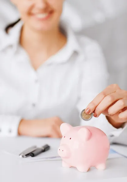 Женщина руку положить монету в малых Копилка — стоковое изображение Женщина руку положить монету в малых Копилка — стоковое фото